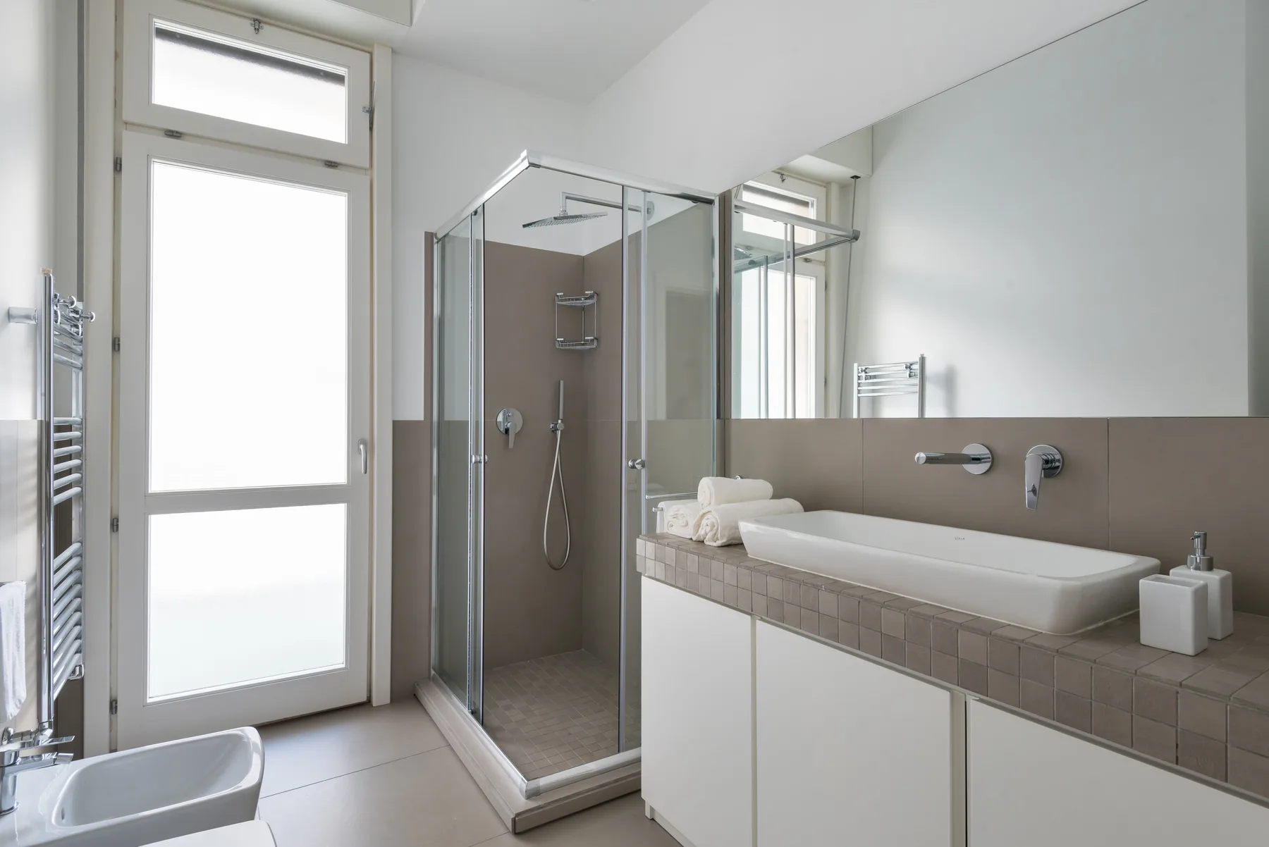 A bright modern bathroom with a glass shower and a long sink counter.