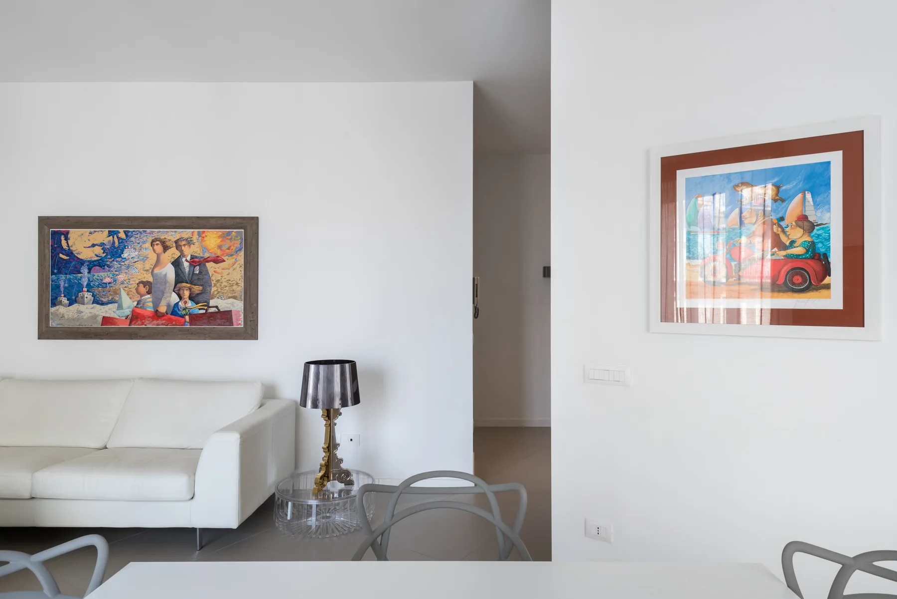 A bright living room with white seating and colorful framed artwork.