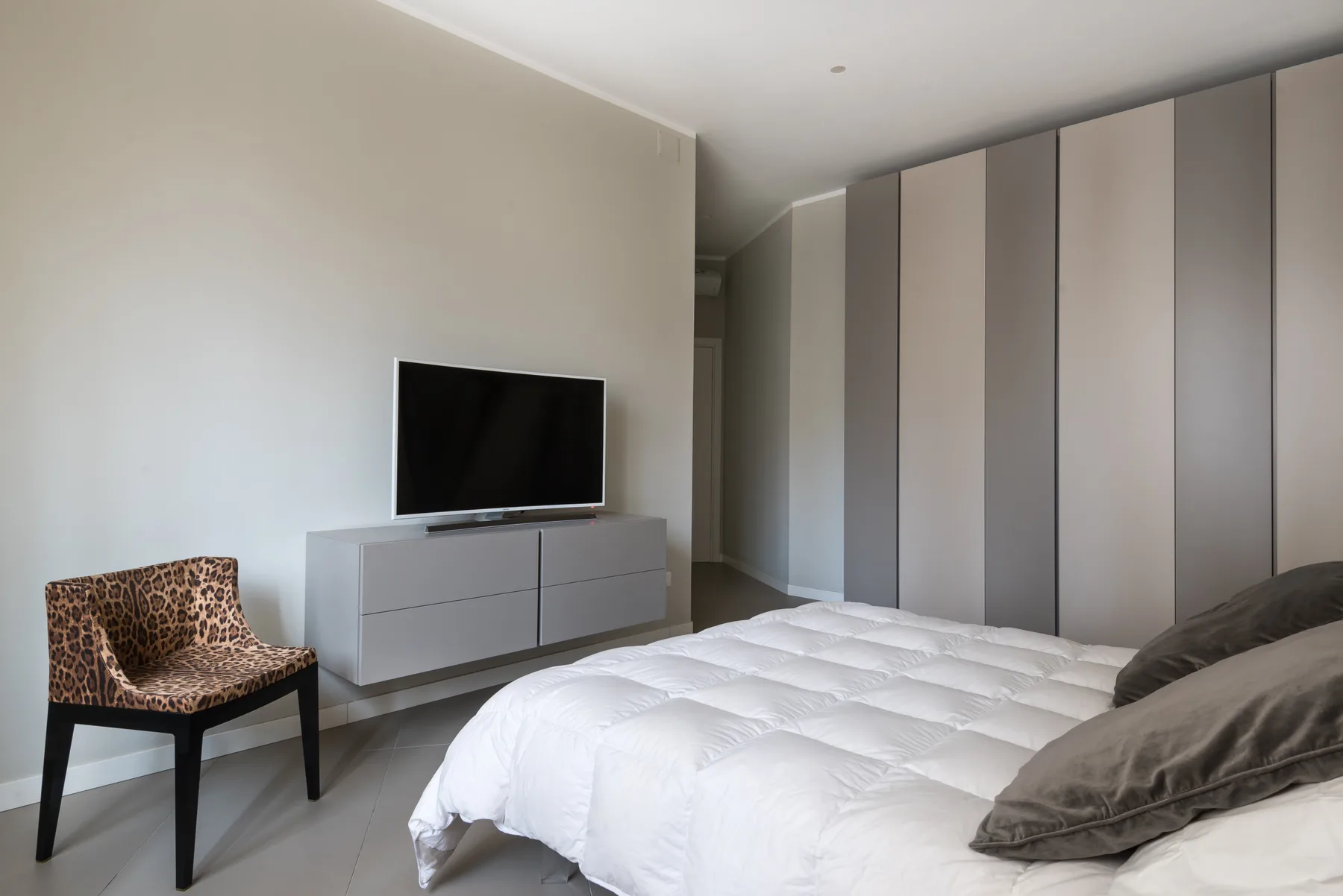 A bright bedroom with a white bed, television, and built-in wardrobes.