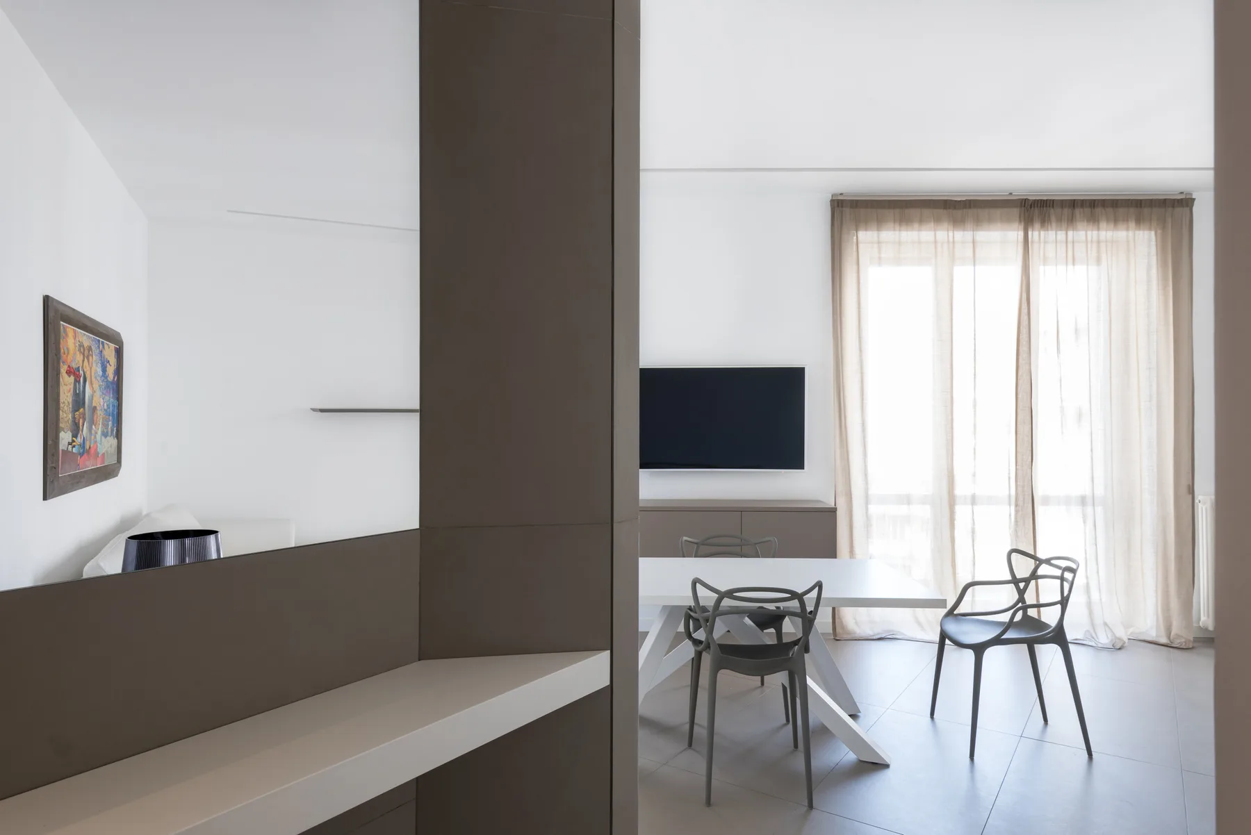 A modern living and dining area with a television and table beside curtained windows.