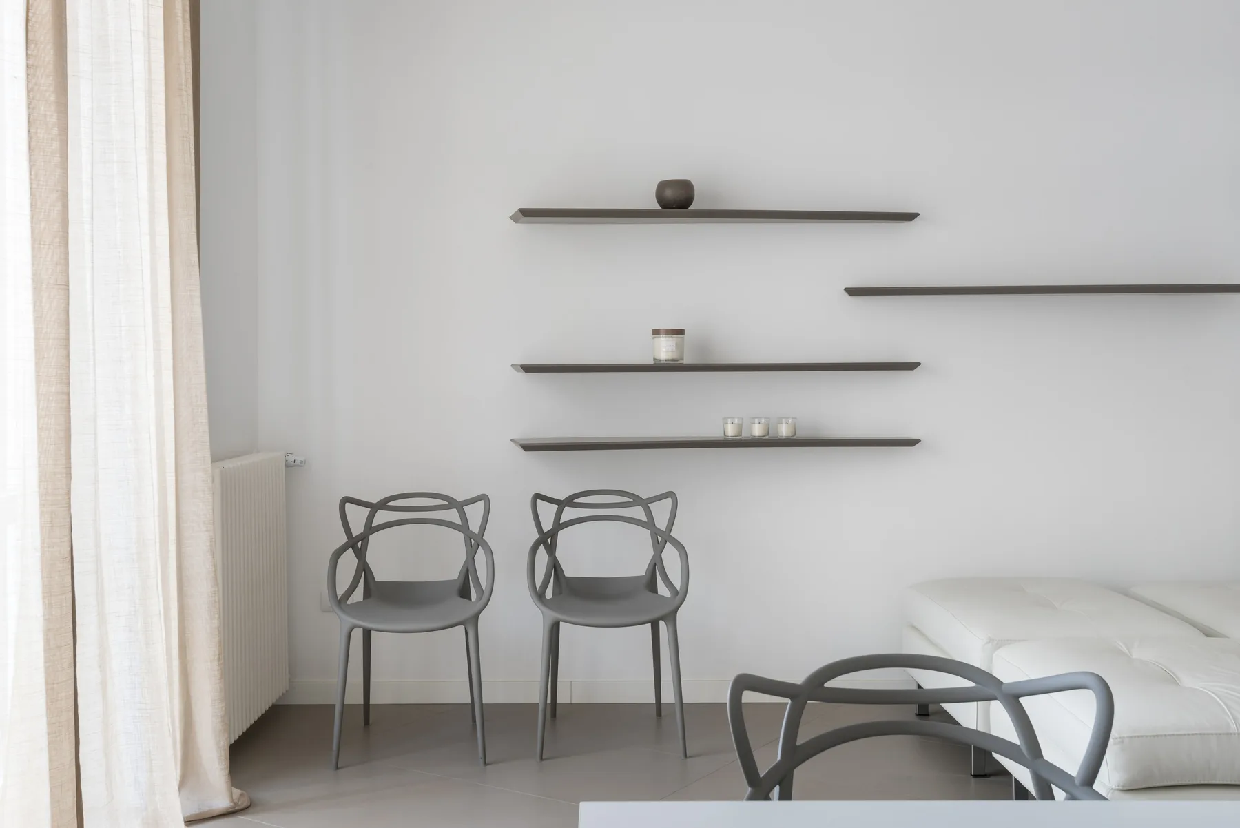 A bright bedroom with seating beneath three wall shelves.