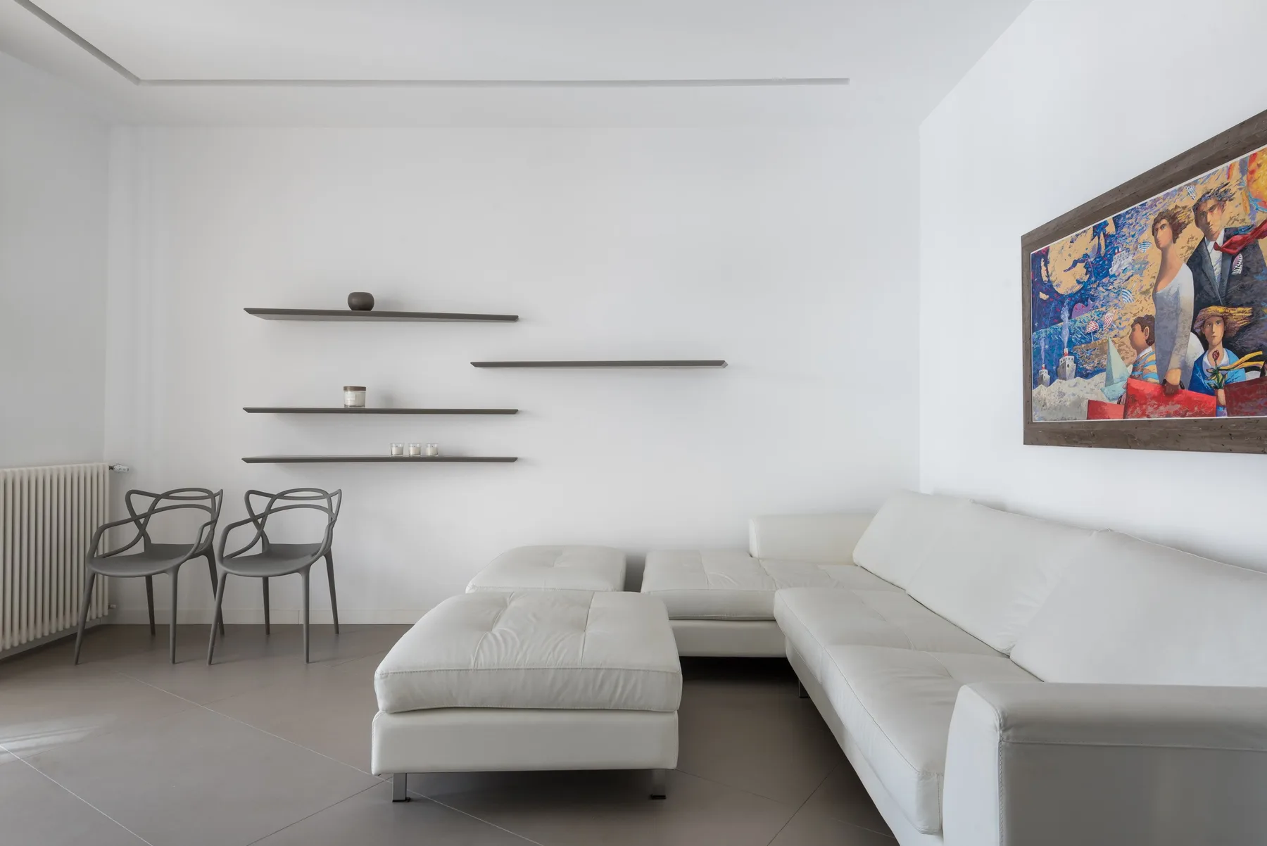 A bright living room with white seating and framed artwork on the wall.