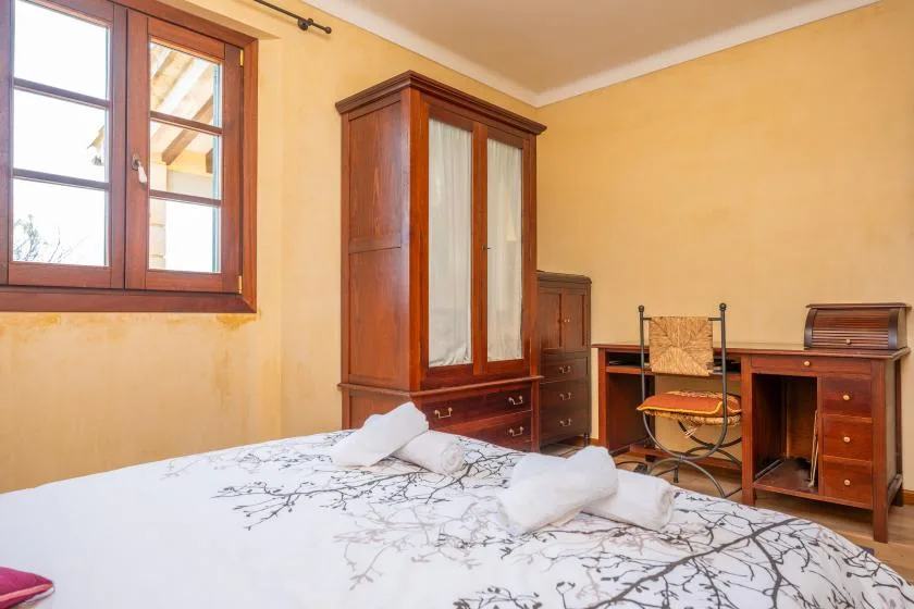 Un dormitorio con una cama, un armario de madera y un escritorio junto a una ventana.