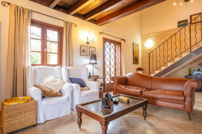 Una sala de estar con sillones blancos, un sofá marrón y una escalera.