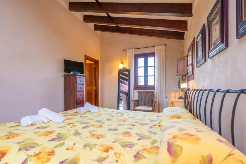 Un dormitorio con una colcha floral, una ventana y vigas de techo a la vista.