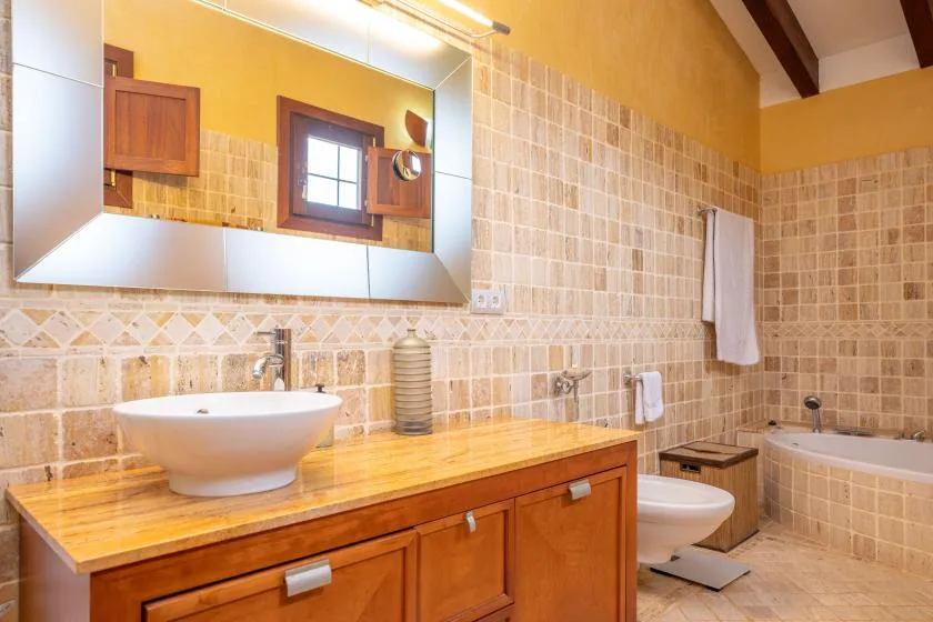 Un baño alicatado con un espejo amplio sobre un tocador de madera y lavabo.