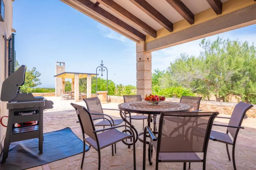 Un patio exterior cubierto tiene una mesa de comedor, asientos y una parrilla.