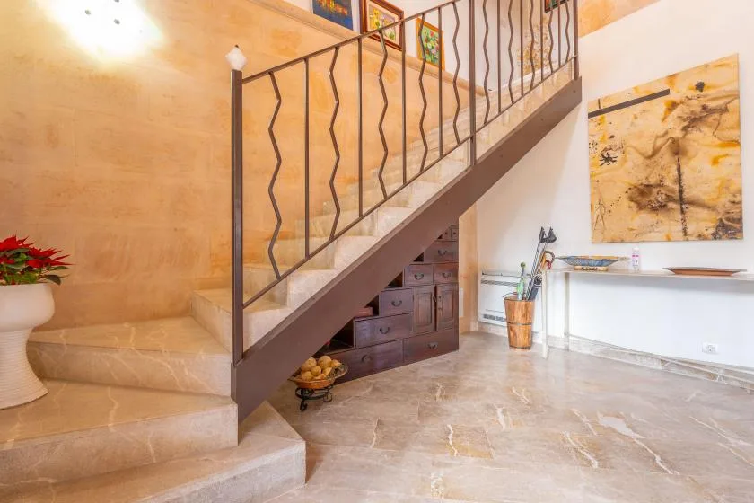 Una escalera interior luminosa con barandilla oscura y obras de arte en la pared.