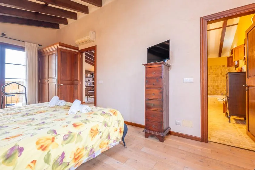 Un dormitorio con una colcha floral y un televisor sobre una cómoda de madera.