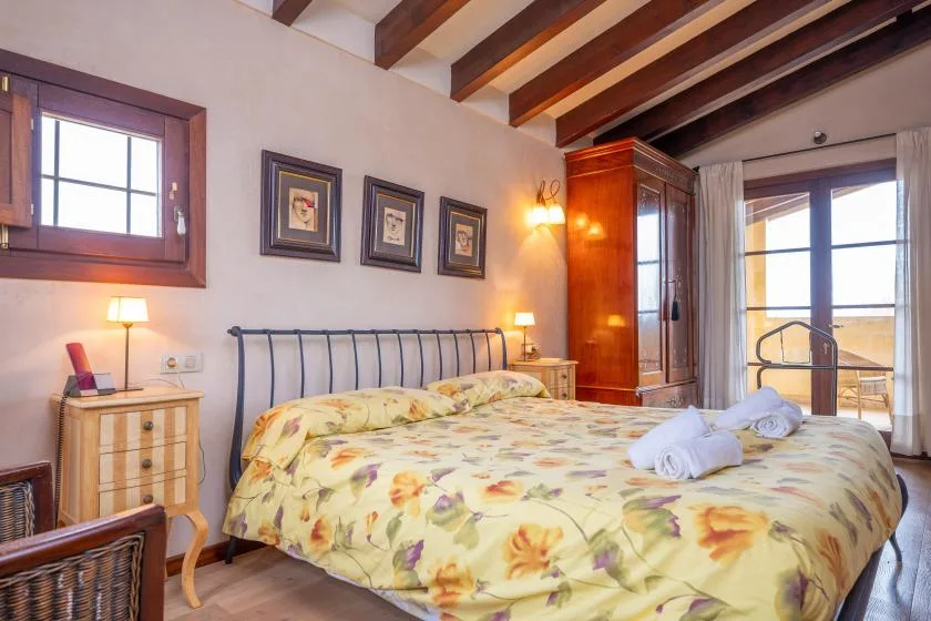 Un dormitorio con una colcha floral, mesitas de noche y vigas de techo a la vista.