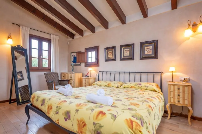 Un dormitorio con una colcha floral, cuadros enmarcados y vigas expuestas en el techo.