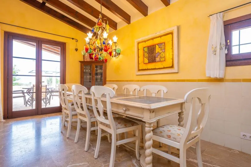 Comedor con una mesa larga y sillas bajo una lámpara de araña colorida.