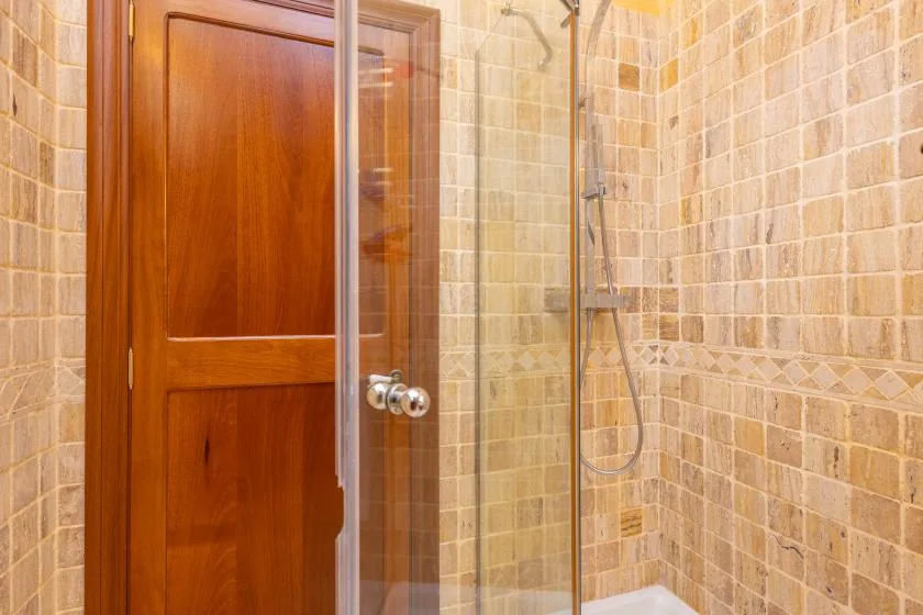 Un baño alicatado con una puerta de madera y una ducha de vidrio.