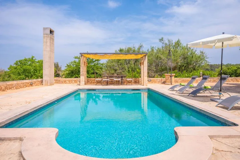 Una piscina al aire libre junto a una pérgola sombreada y asientos de descanso.