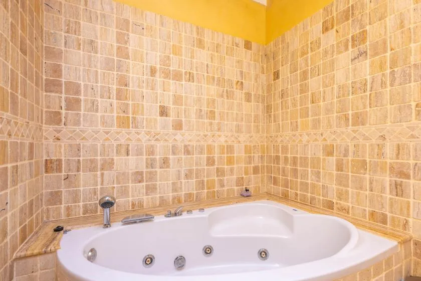 Una bañera de esquina está junto a paredes de azulejos en un baño.