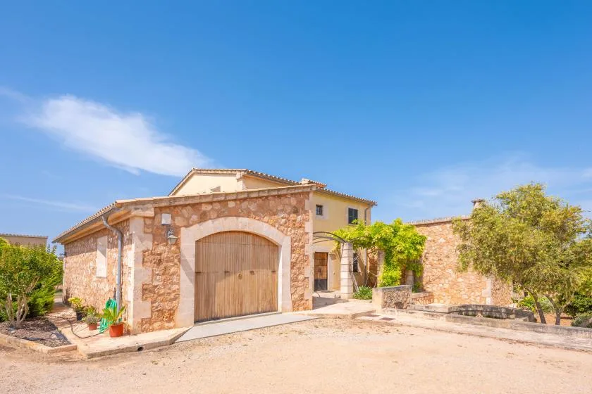 La entrada de una casa de piedra con un gran portón de madera y jardín alrededor.