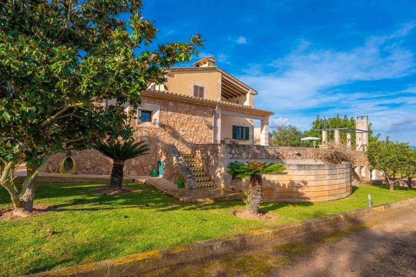 Una casa de piedra está junto a un césped y una piscina exterior redonda.