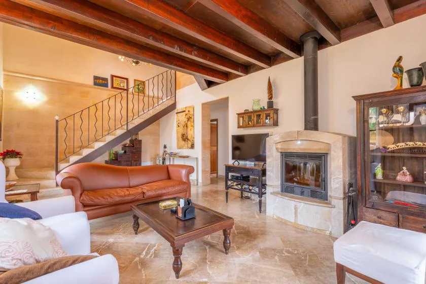 Una sala de estar con asientos, chimenea y escalera bajo vigas de techo expuestas.