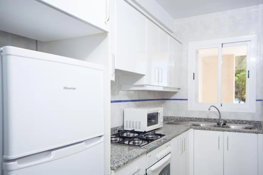 Una cocina luminosa con gabinetes blancos, un refrigerador y un fregadero sobre la encimera.