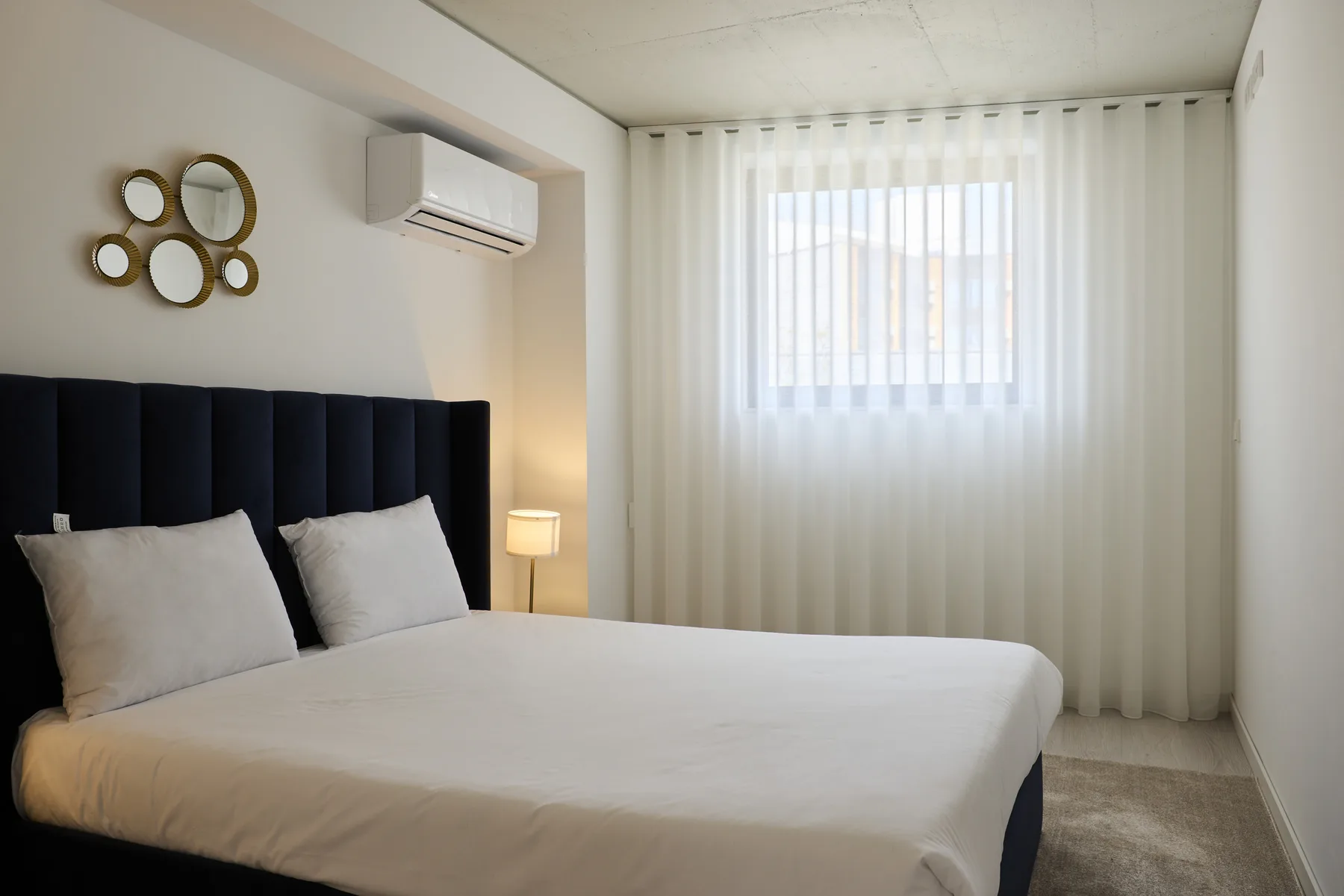 A bedroom with a bed, wall mirrors, and sheer curtains over the window.