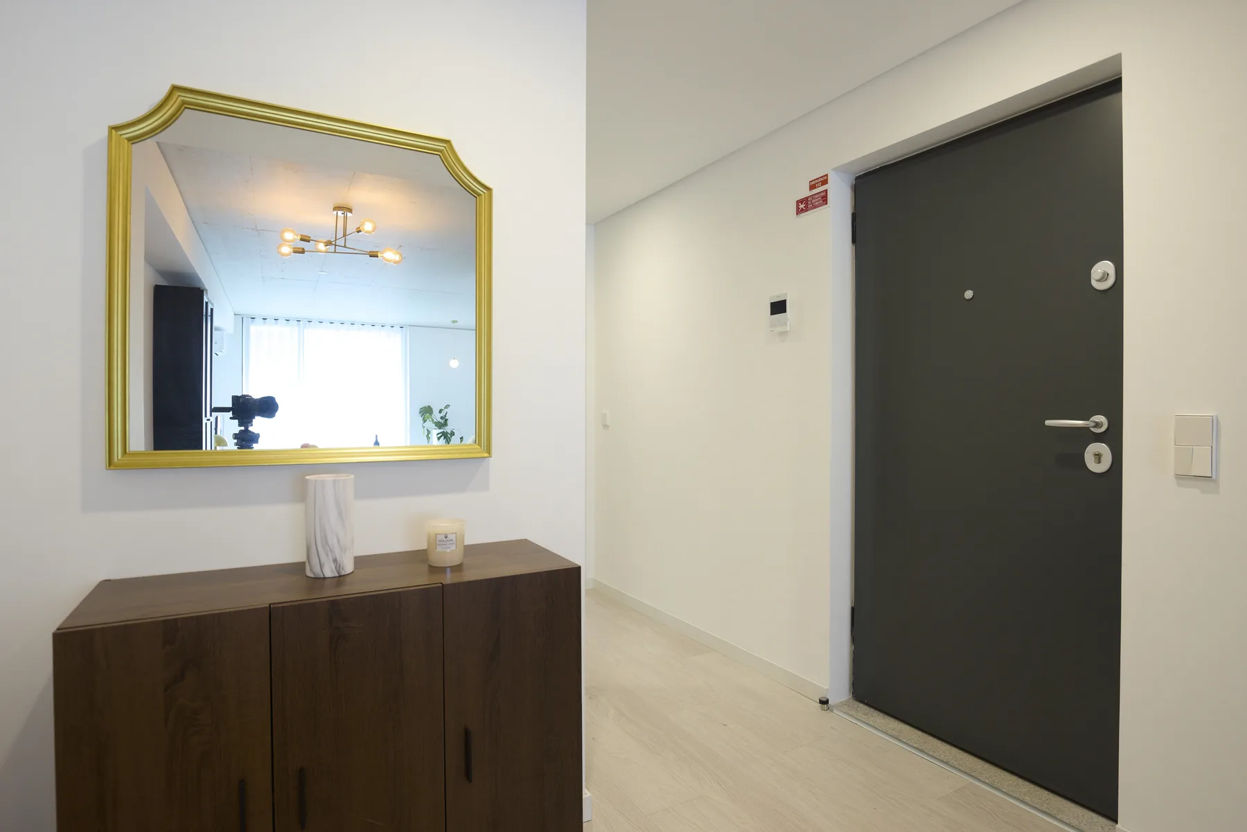 Entrada de un apartamento con una puerta oscura, un mueble de madera y un espejo.