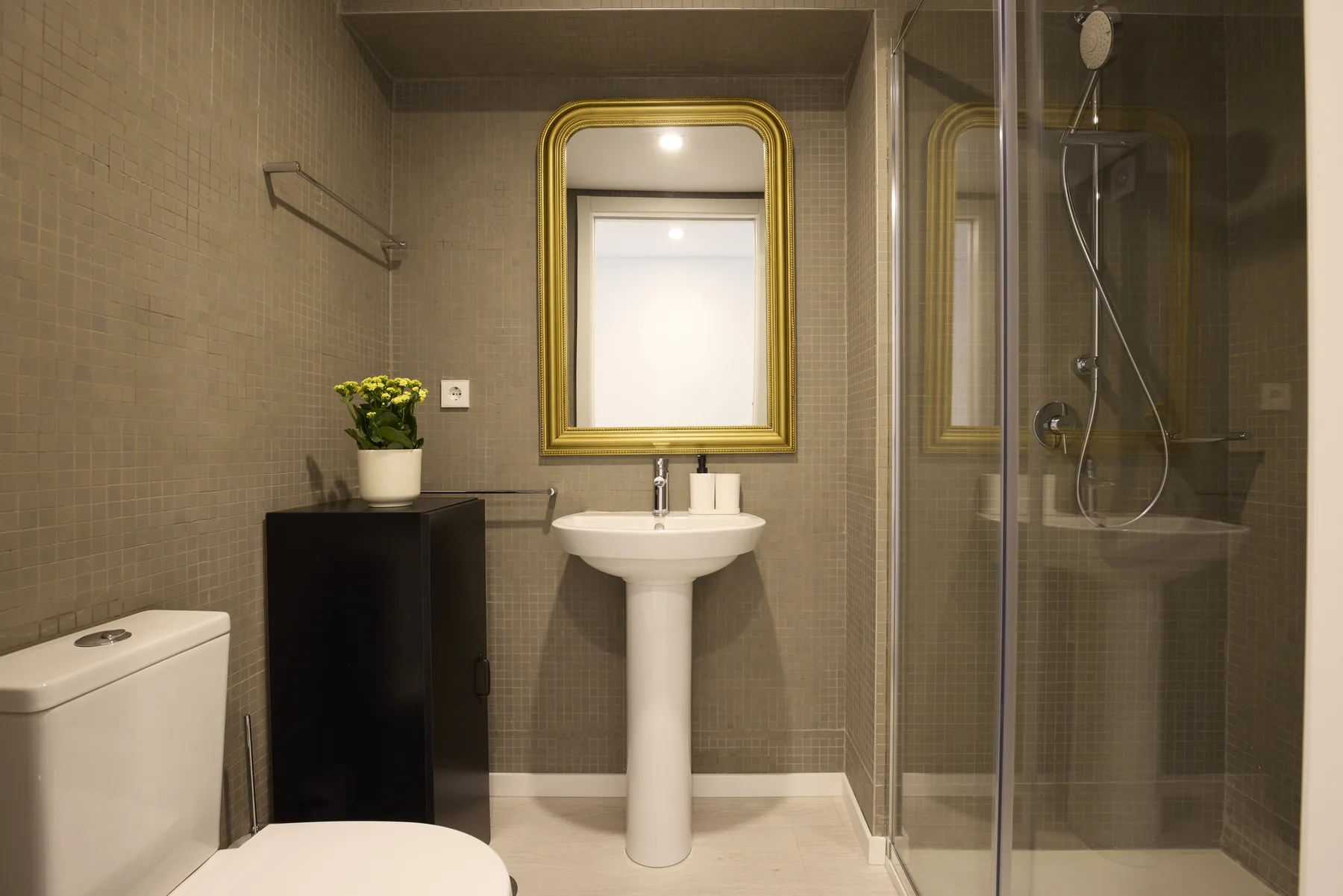 Un baño con lavabo de pedestal, espejo con marco dorado y ducha de vidrio.