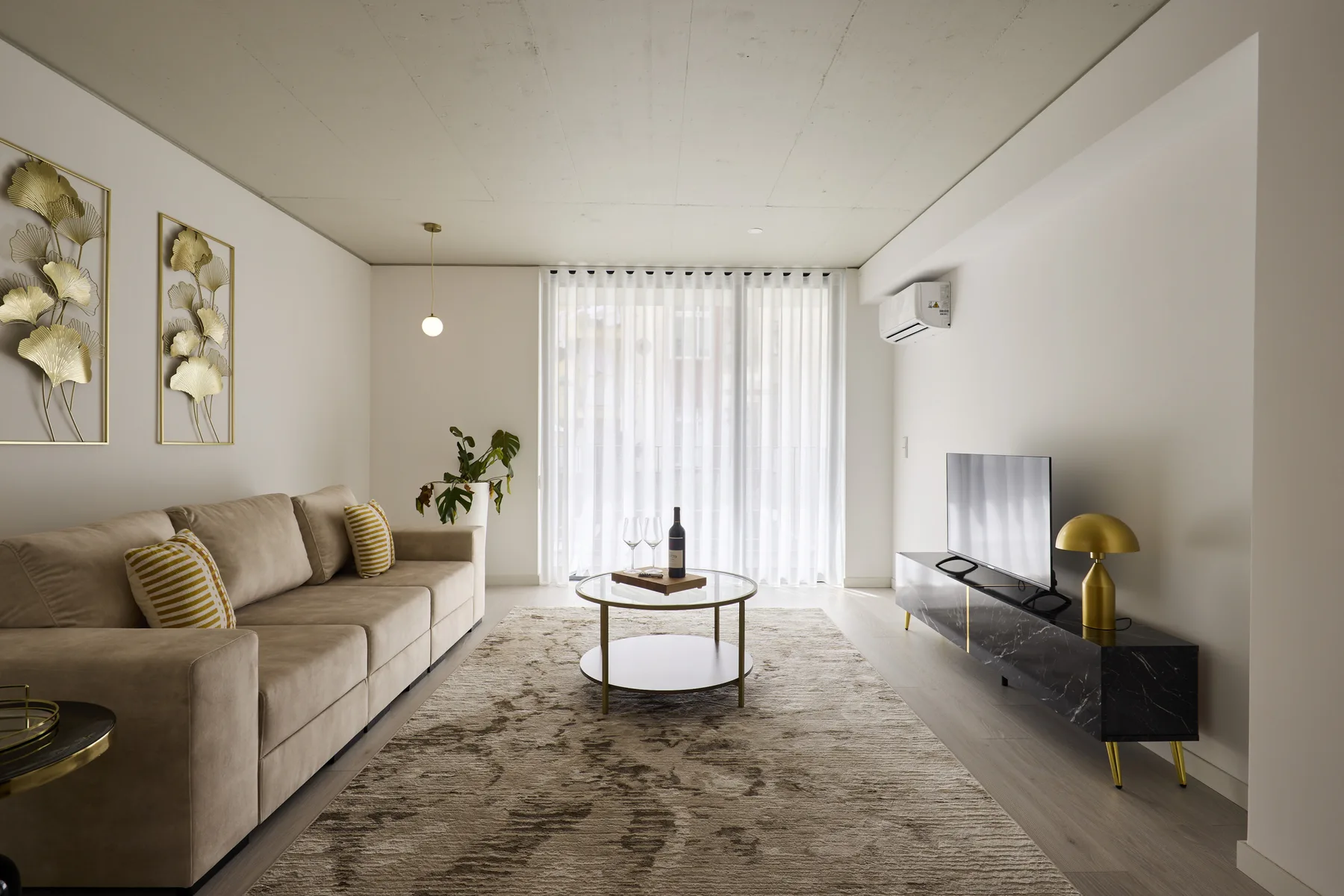A bright living room with seating, a coffee table, and large curtained windows.