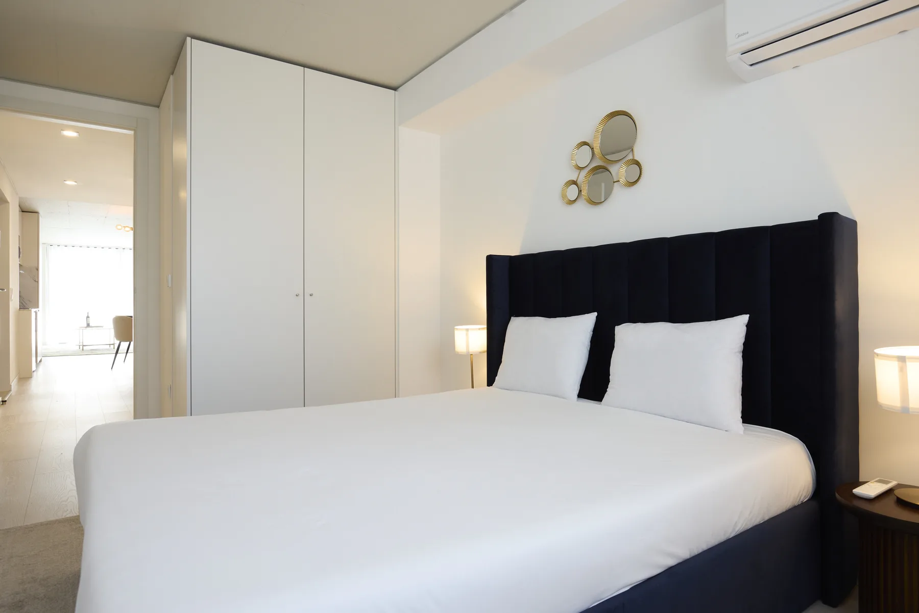 Un dormitorio con una cama blanca y un cabecero alto tapizado en oscuro.