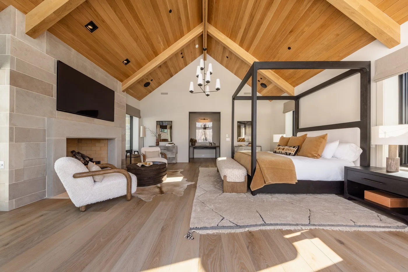 A bedroom with a canopy bed, seating area, and vaulted wood ceiling.