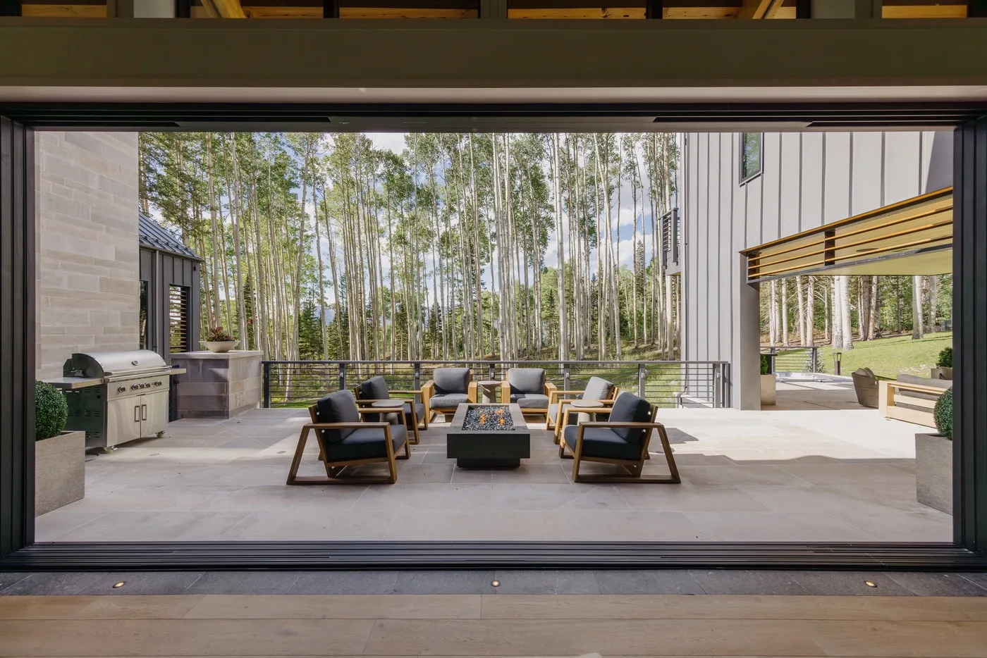An outdoor patio with lounge seating and a wooded view beyond.