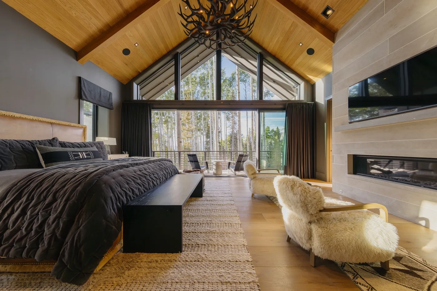 A spacious bedroom with a bed, tall windows, and a vaulted wooden ceiling.