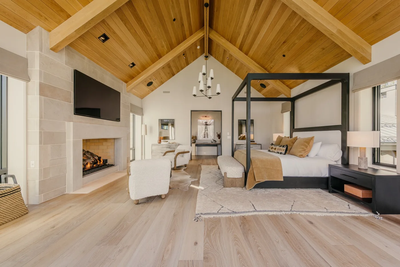 A spacious bedroom with a canopy bed, fireplace, and vaulted wood ceiling.
