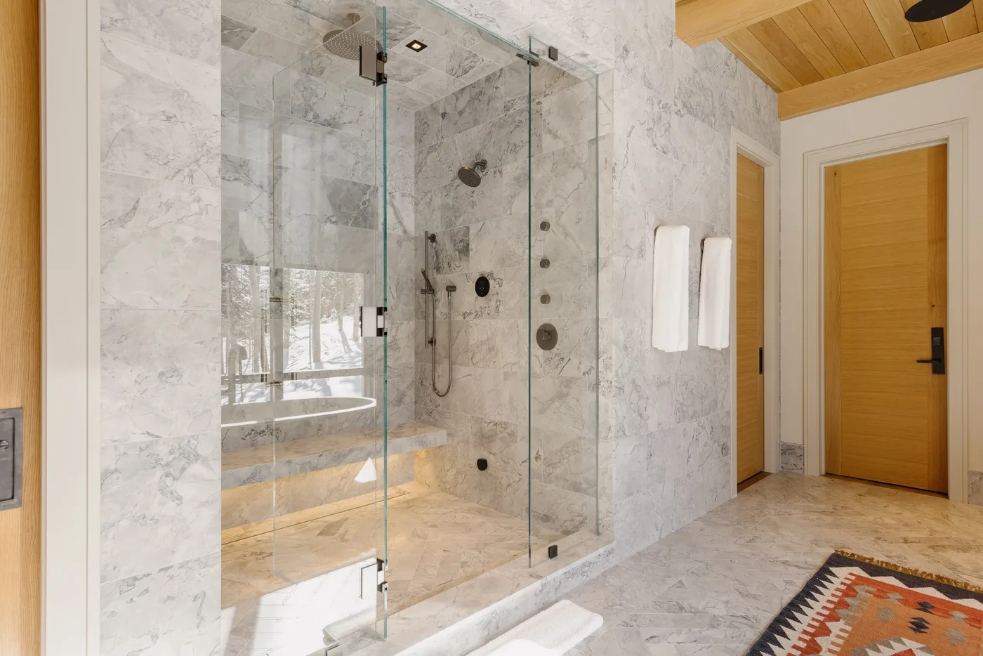 A marble bathroom with a glass shower and wooden doors.