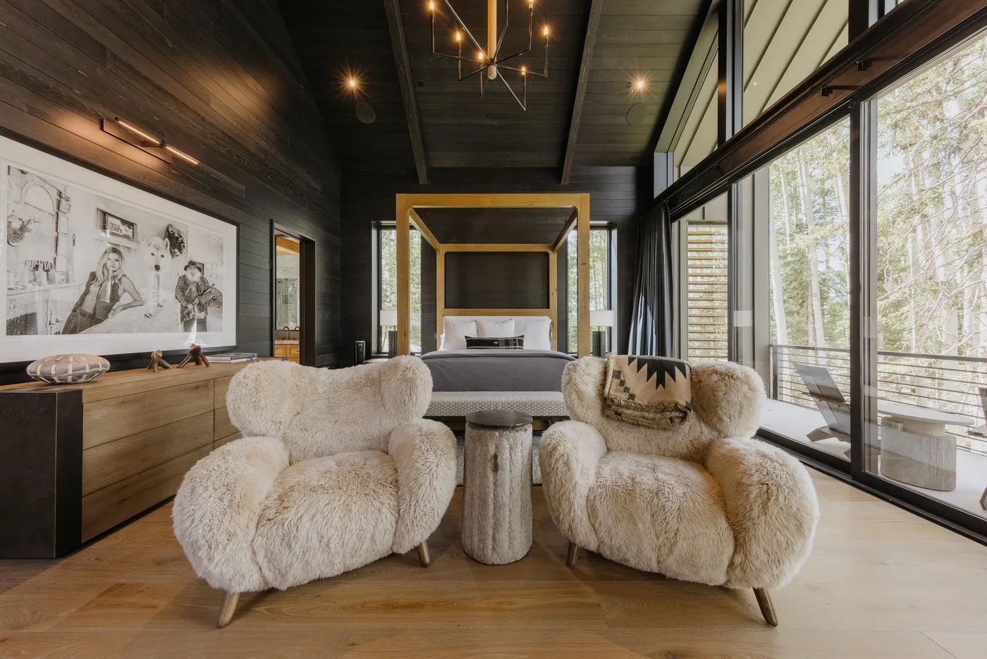 A bedroom with a bed, two plush armchairs, and large windows.