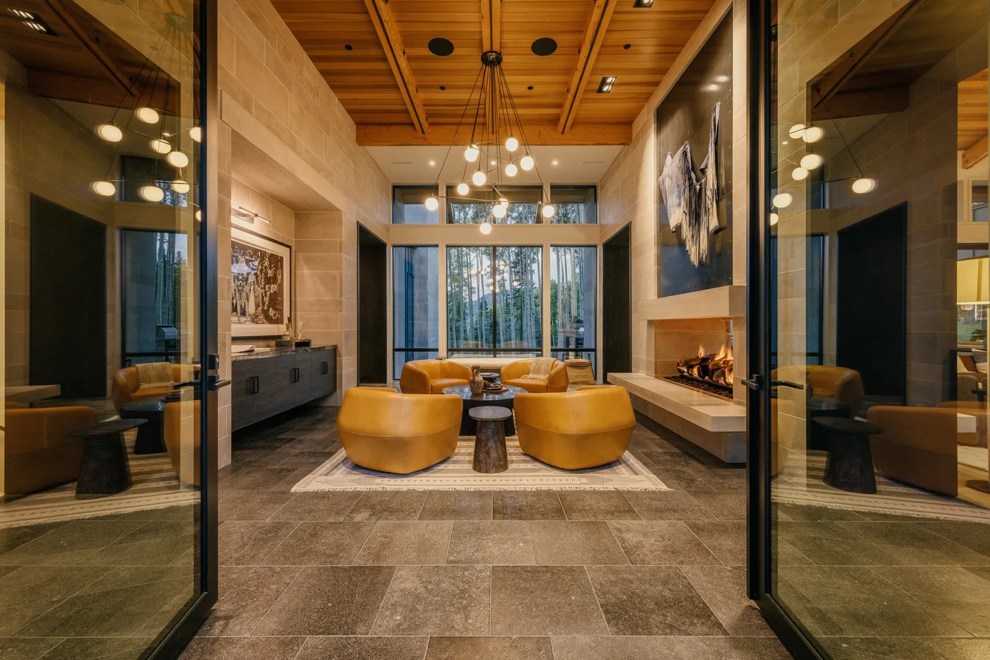 A modern living room with seating arranged around a fireplace and large windows.
