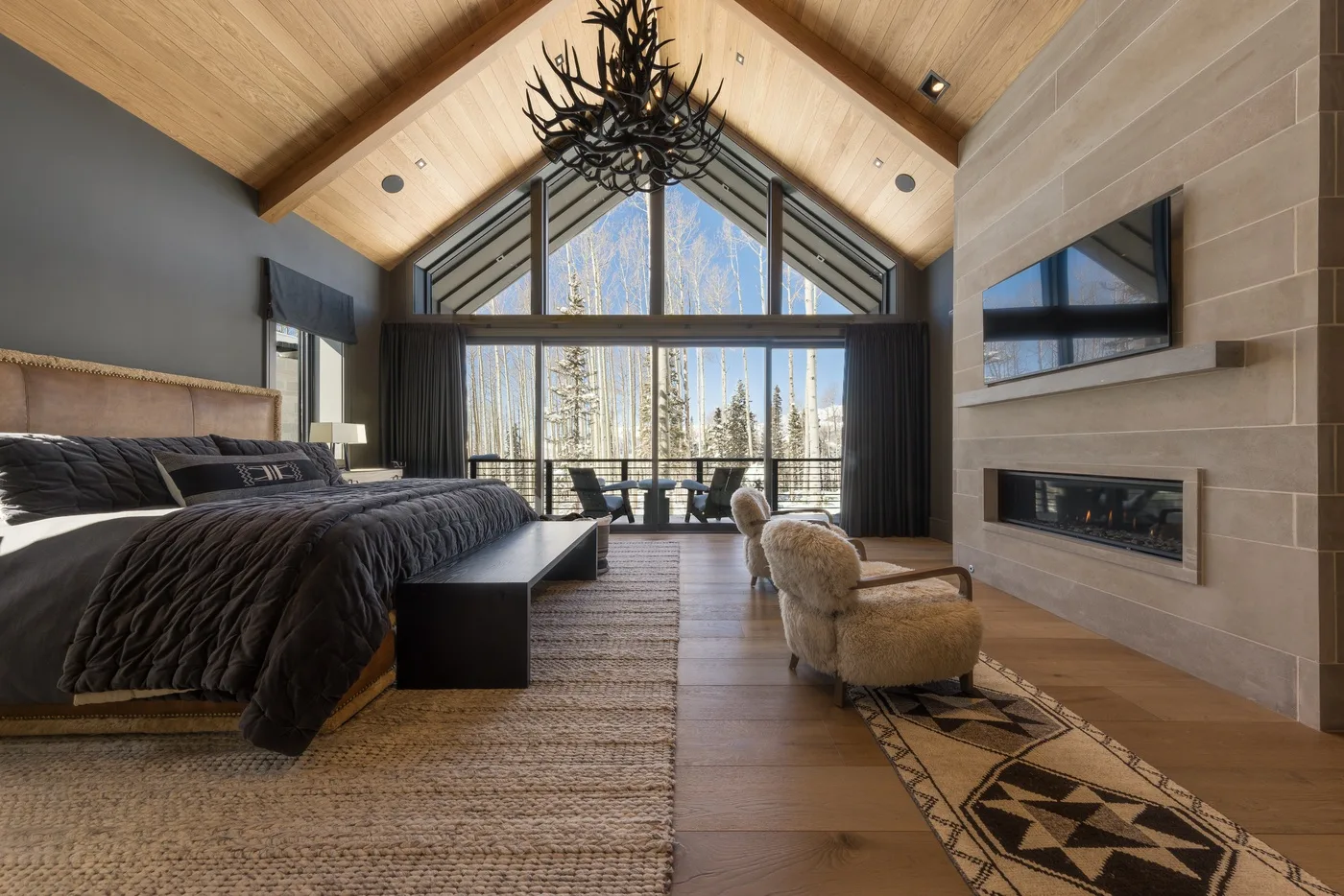 A bedroom with a large bed, lounge seating, and expansive windows.