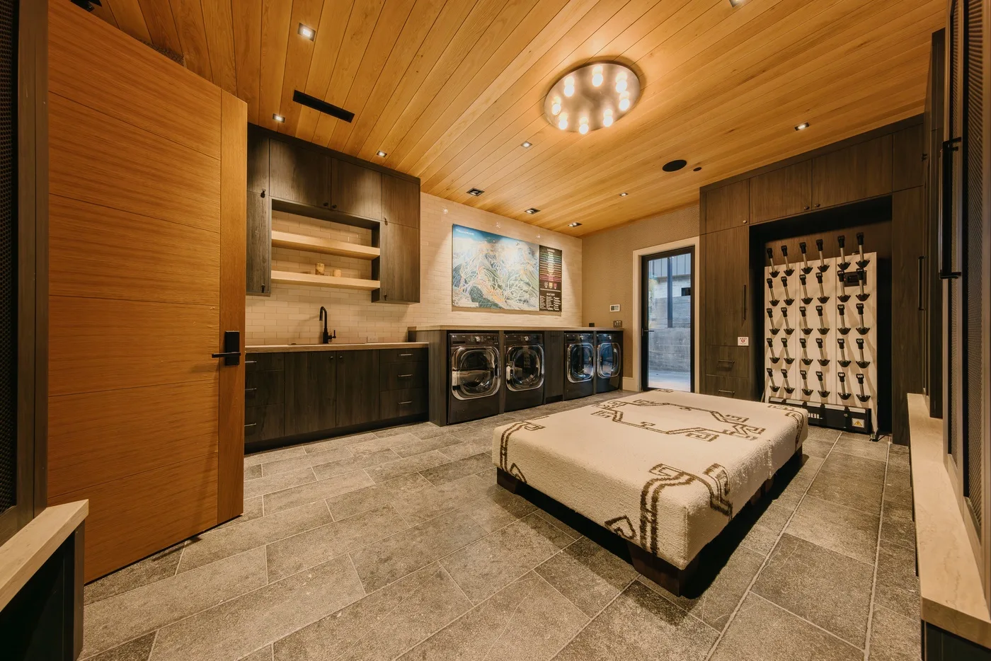 A bedroom with a bed, laundry machines, and warm wood-paneled walls.