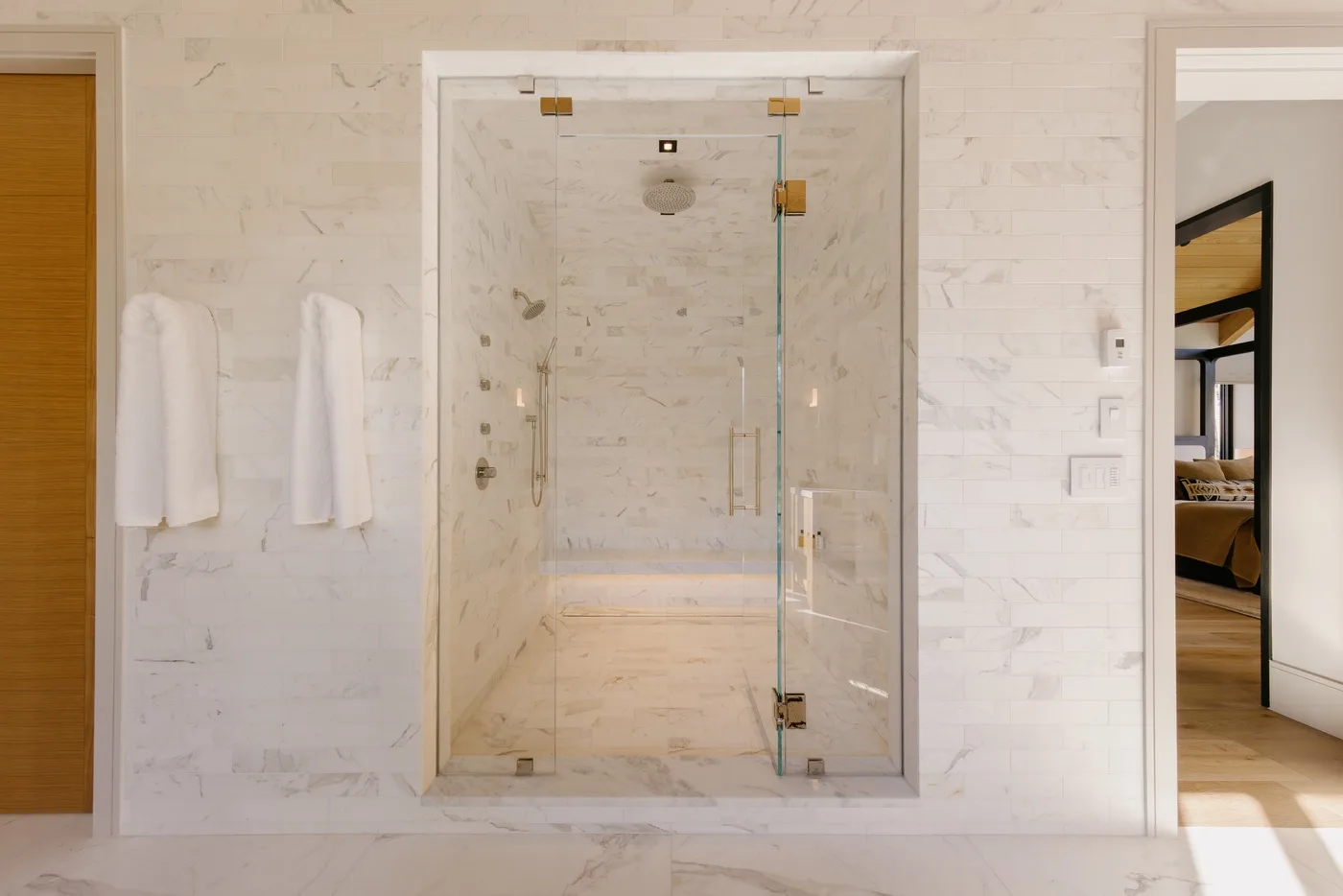 A tiled bathroom with a glass shower and white towels hanging on the wall.