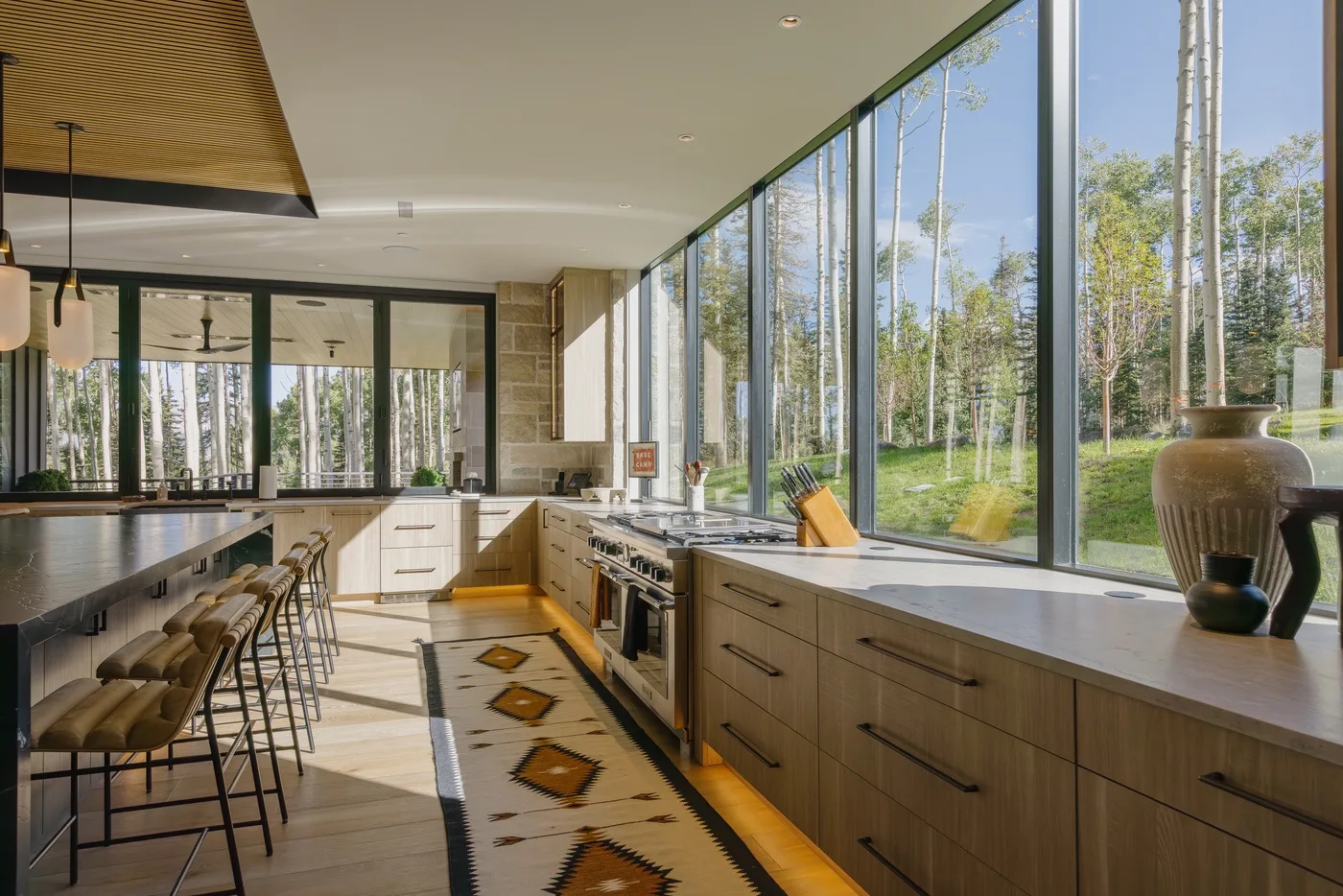 A bright kitchen with a long island and large windows overlooking trees.