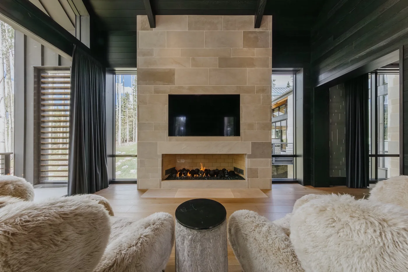 A living room with a stone fireplace and television between large windows.