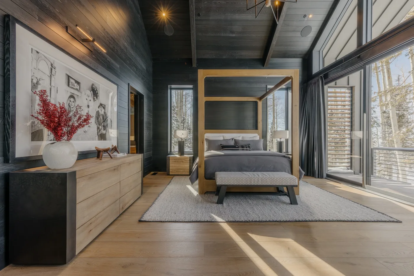 A bedroom with a bed, a wooden dresser, and large windows.