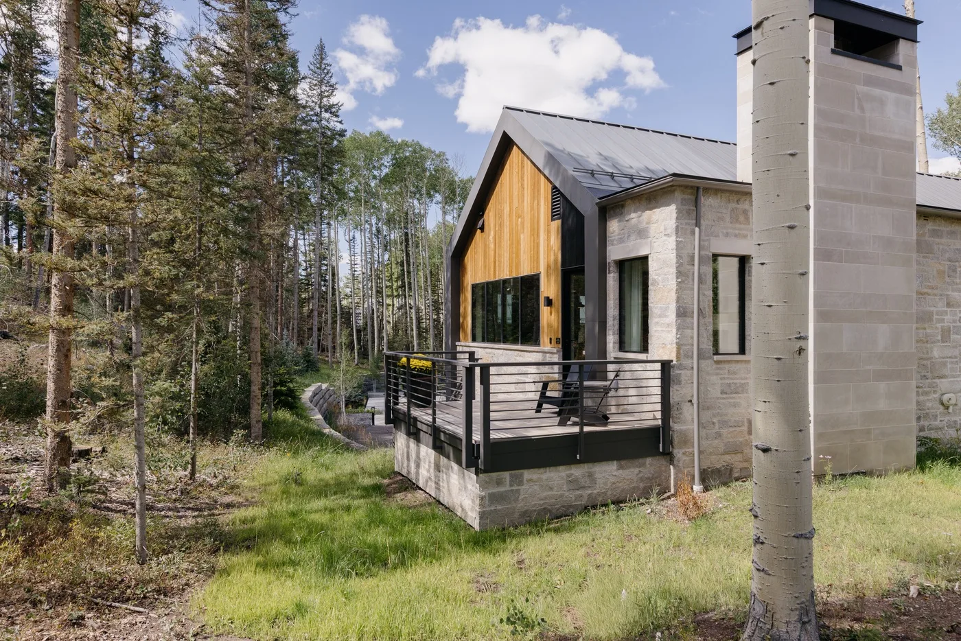A modern house with a raised deck sits among trees.