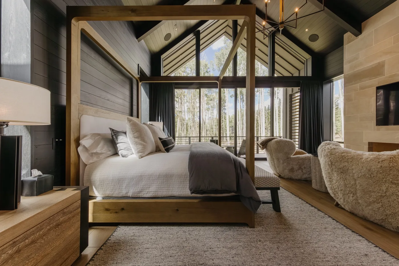 A bedroom with a wooden canopy bed, plush seating, and tall windows.