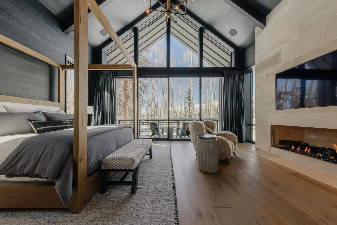 A bedroom with a high sloped ceiling, large windows, and a fireplace.