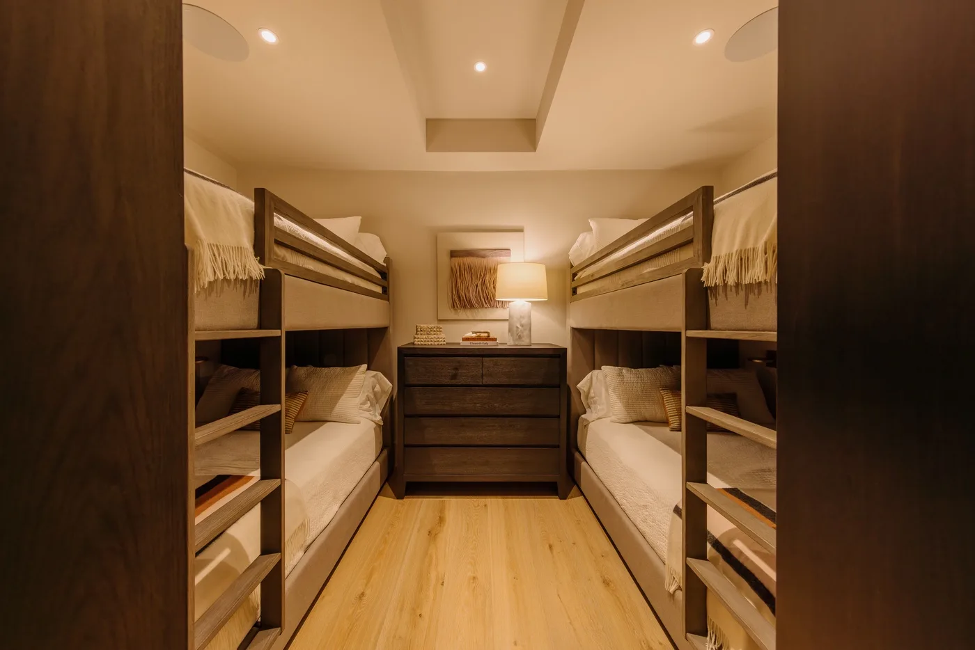 A bedroom with two bunk beds facing a dark chest of drawers.