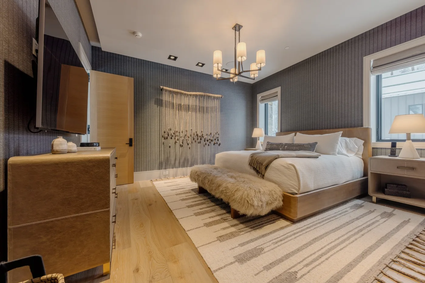 A bedroom with a large bed, a bench, and a striped rug.