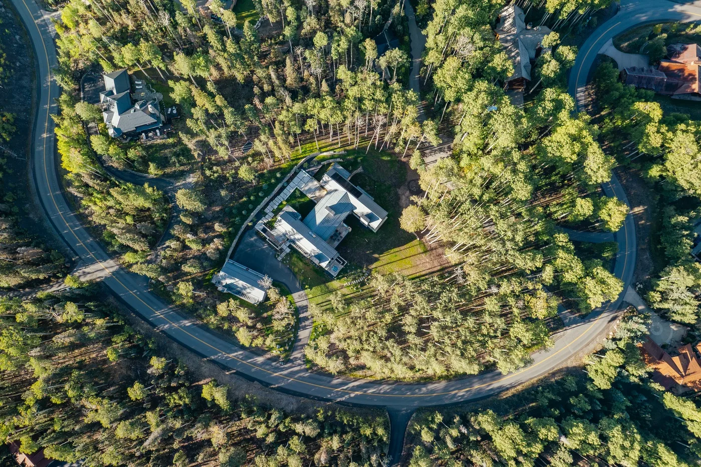 Aerial view of a house surrounded by dense trees and a winding road.