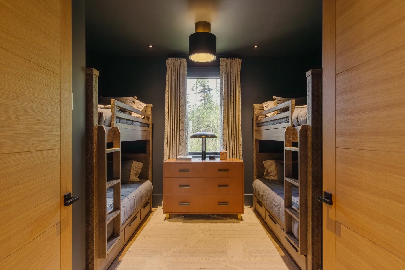 A bedroom with two bunk beds and a dresser beneath a central window.