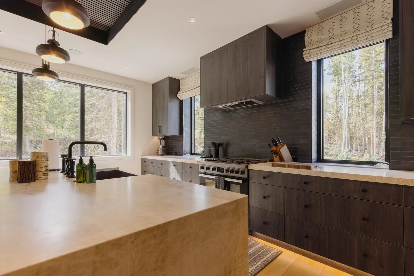 A modern kitchen with dark cabinetry, a large island, and wide windows.
