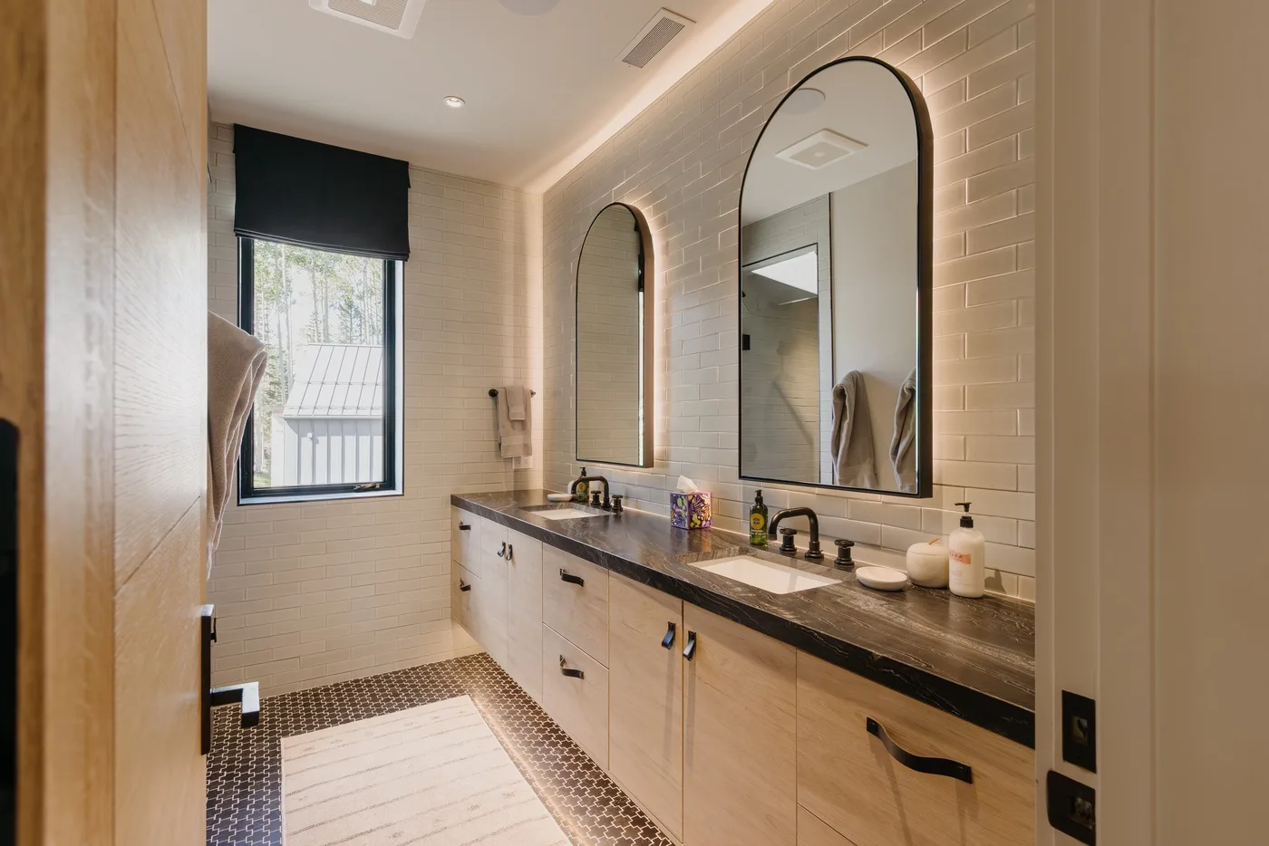 A bathroom vanity with mirrors, sinks, and a window.